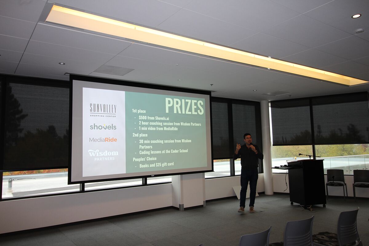 An organizer stands beside the projected PRIZES slide, which lists first- and second-place awards alongside the sponsor logos.