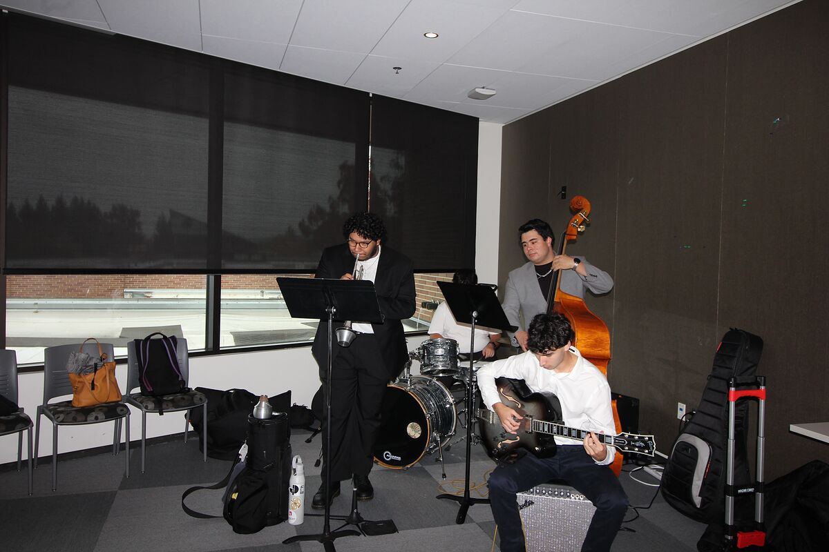 A student jazz combo — upright bass, electric guitar, drums, and a vocalist at a music stand — plays at the side of the room.